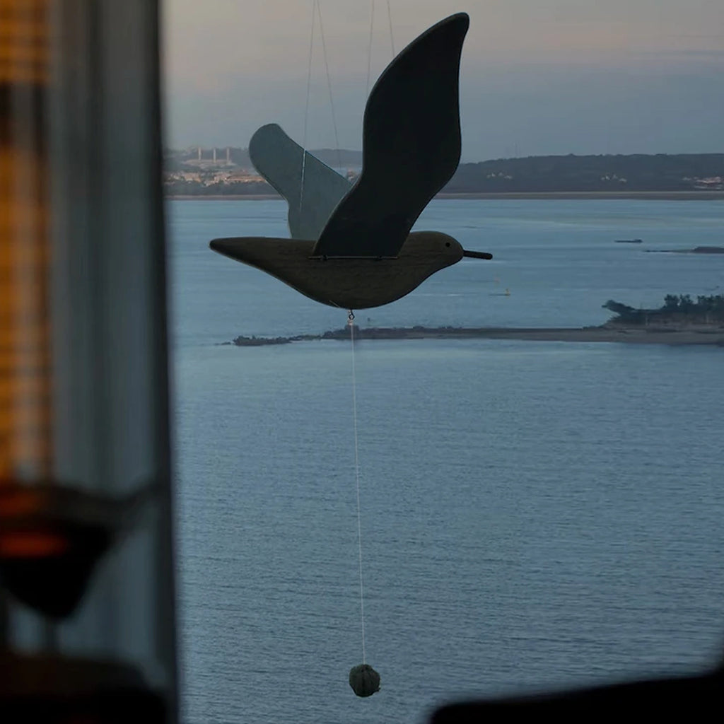 Silhouette view of the wooden seagull mobile against the ocean at dusk.