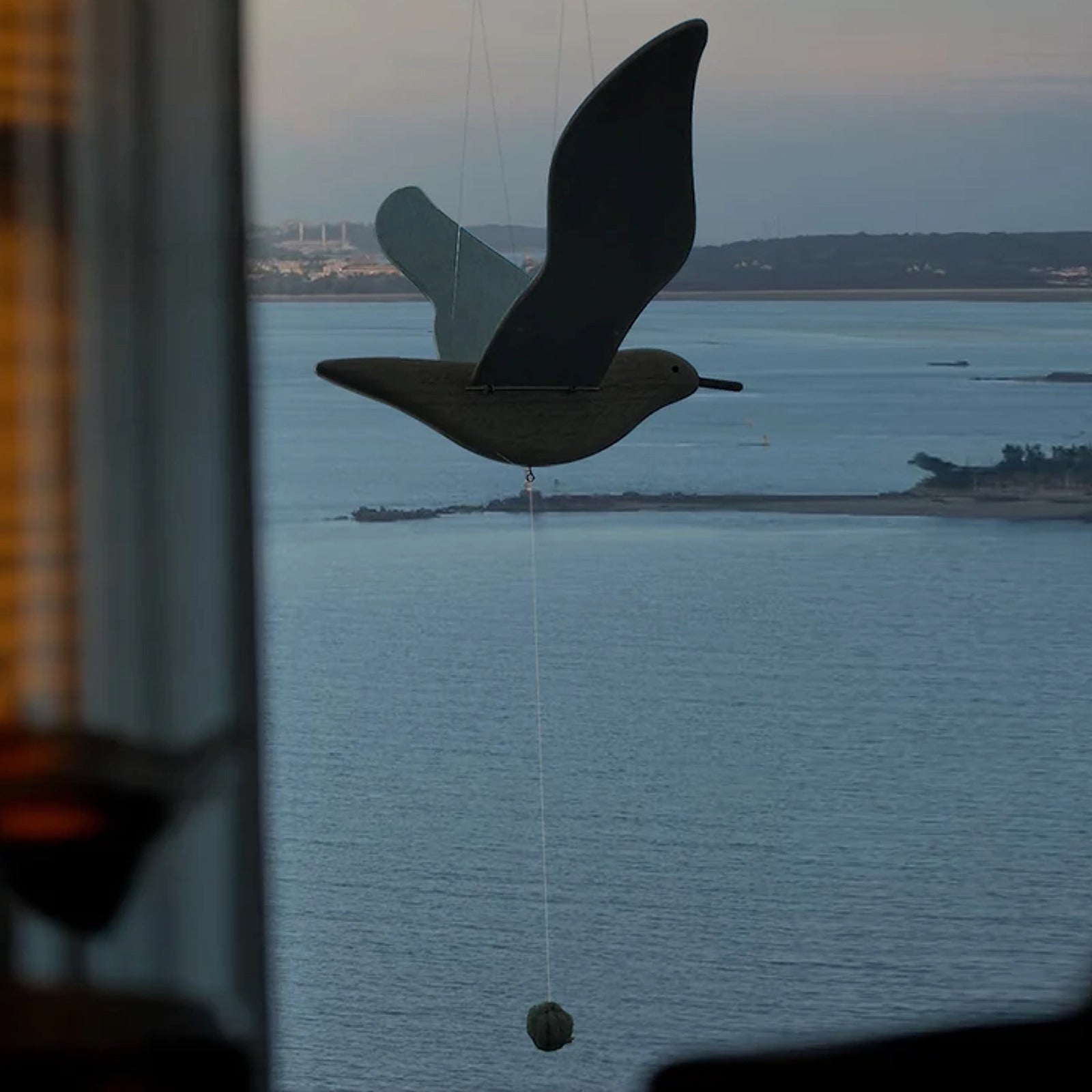 Silhouette view of the wooden seagull mobile against the ocean at dusk.